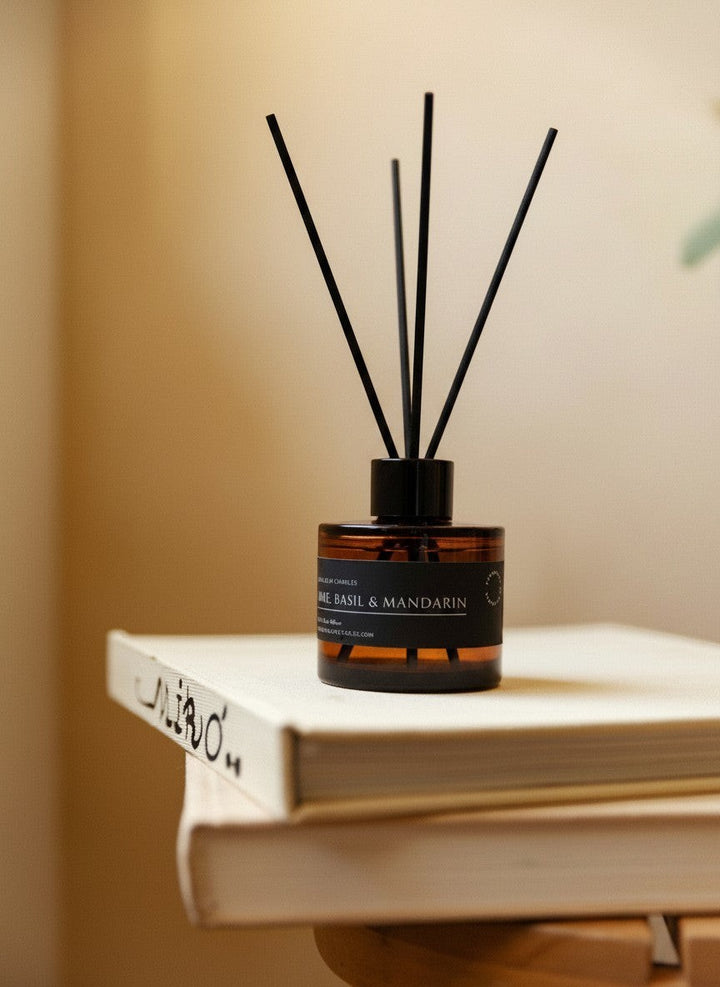 Glim & Glam Lime, Basil & Mandarin reed diffuser in an amber glass bottle with black reeds resting on a stack of books.