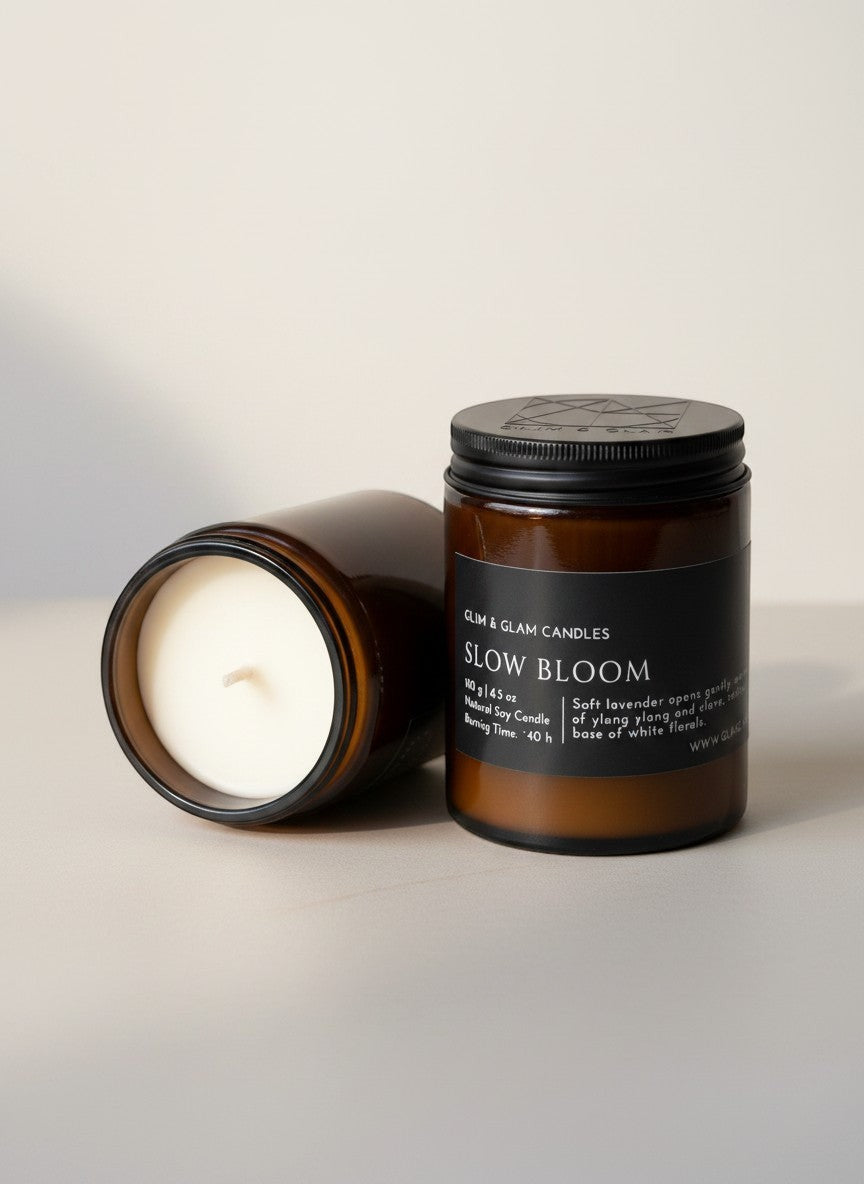 Glim & Glam Slow Bloom soy candle in an amber glass jar with a black lid, featuring lavender and ylang ylang notes.